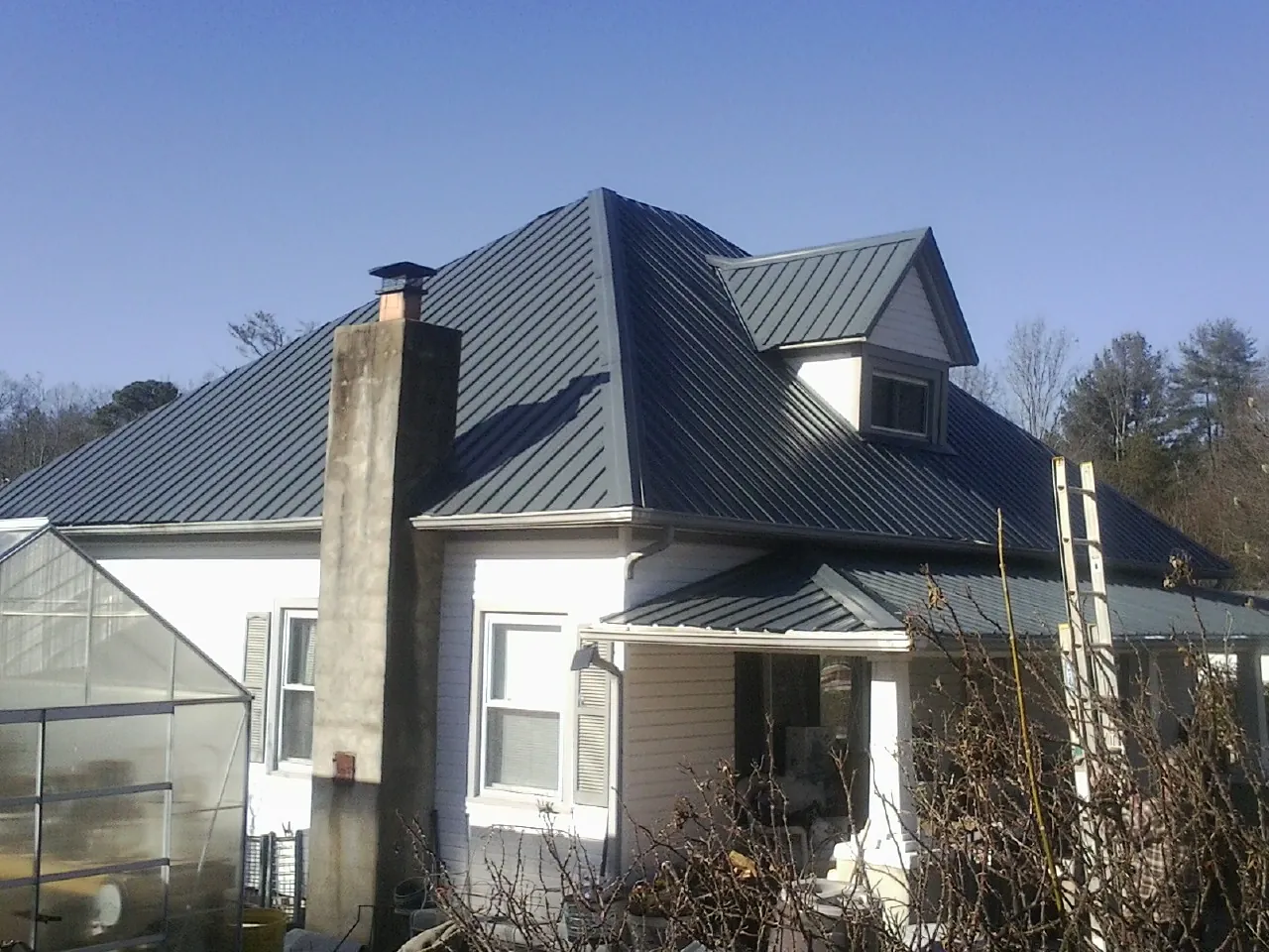 Dark blue standing seam metal roof on a white farmhouse with dormer — Slate & Tile Roof Repair by Roofing Brothers in Green Valley