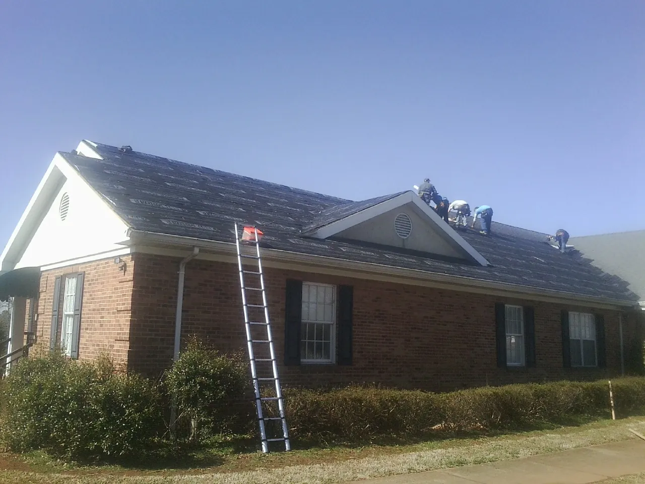 Crew tearing shingles off a brick ranch roof with a ladder set — Metal Roof Repair work by our crew in Green Valley