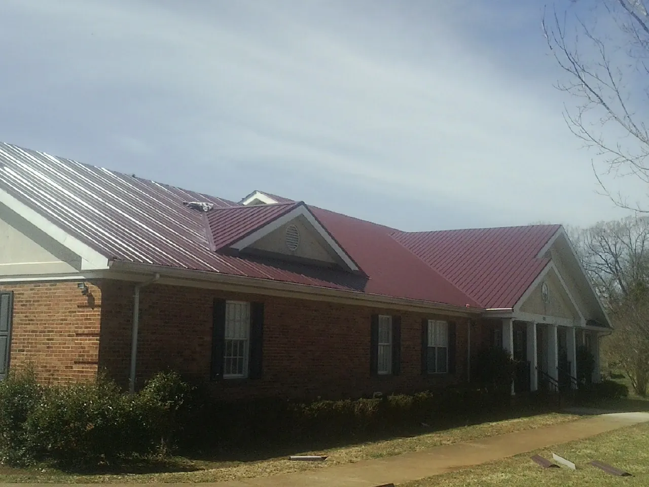 Red metal roof with gabled entries on a long brick building, from a Hail Damage Roof Repair job in Green Valley