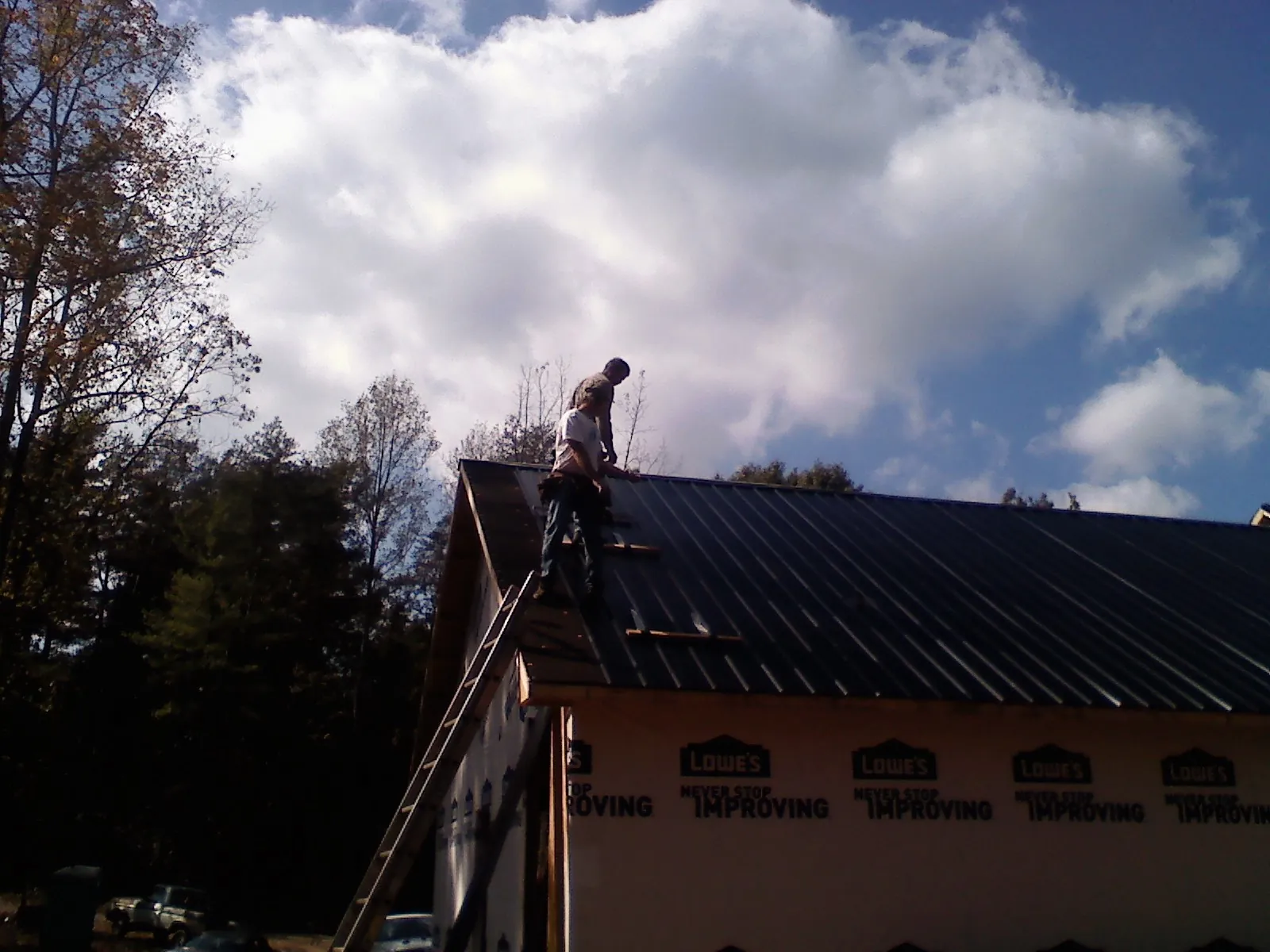 Roofer fastening dark metal panels high against a cloudy sky, from a Roof Inspection job in Green Valley