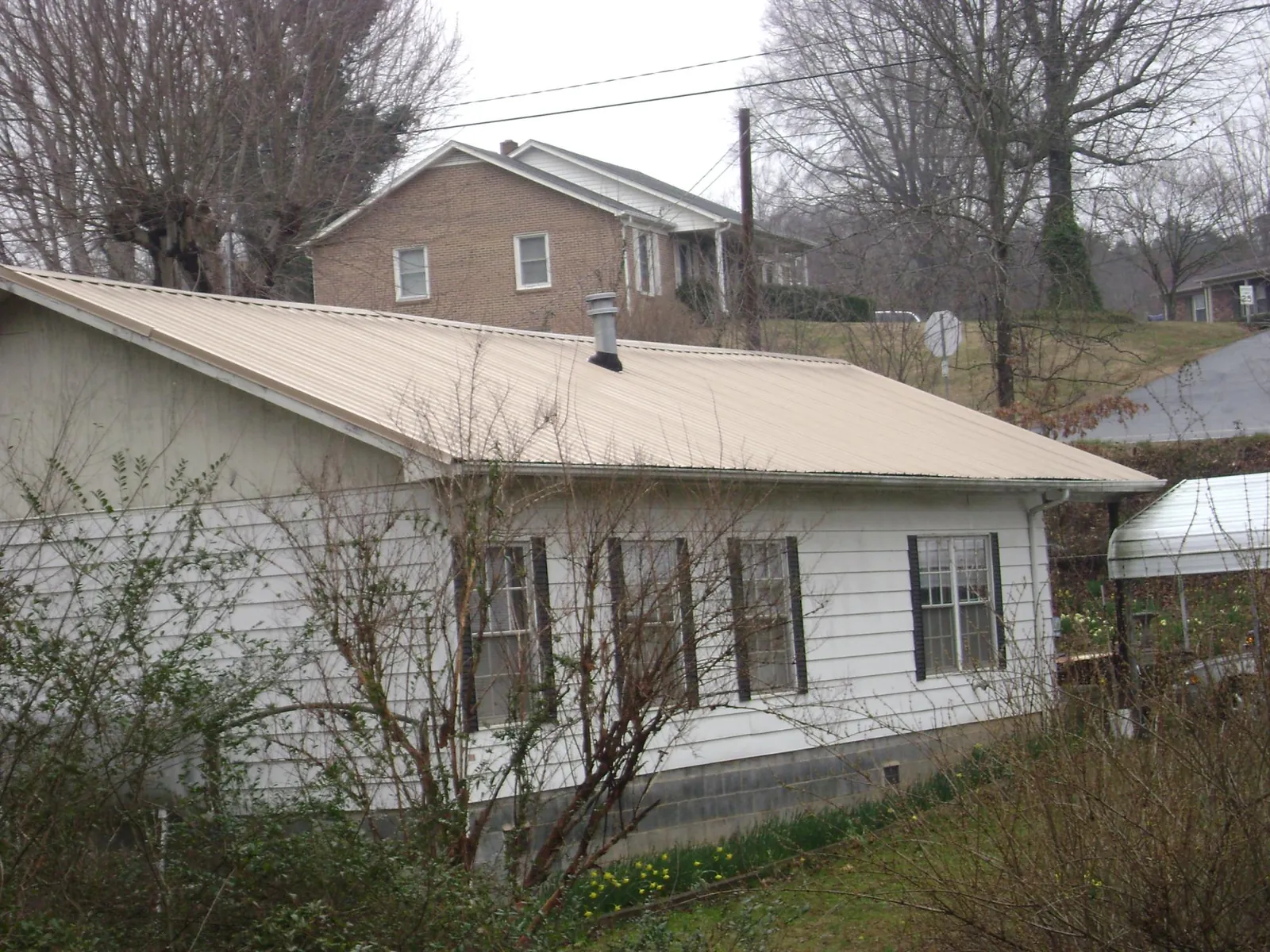 Tan metal roof on a white sided house set into a hillside — Commercial Roofing by Roofing Brothers in Green Valley